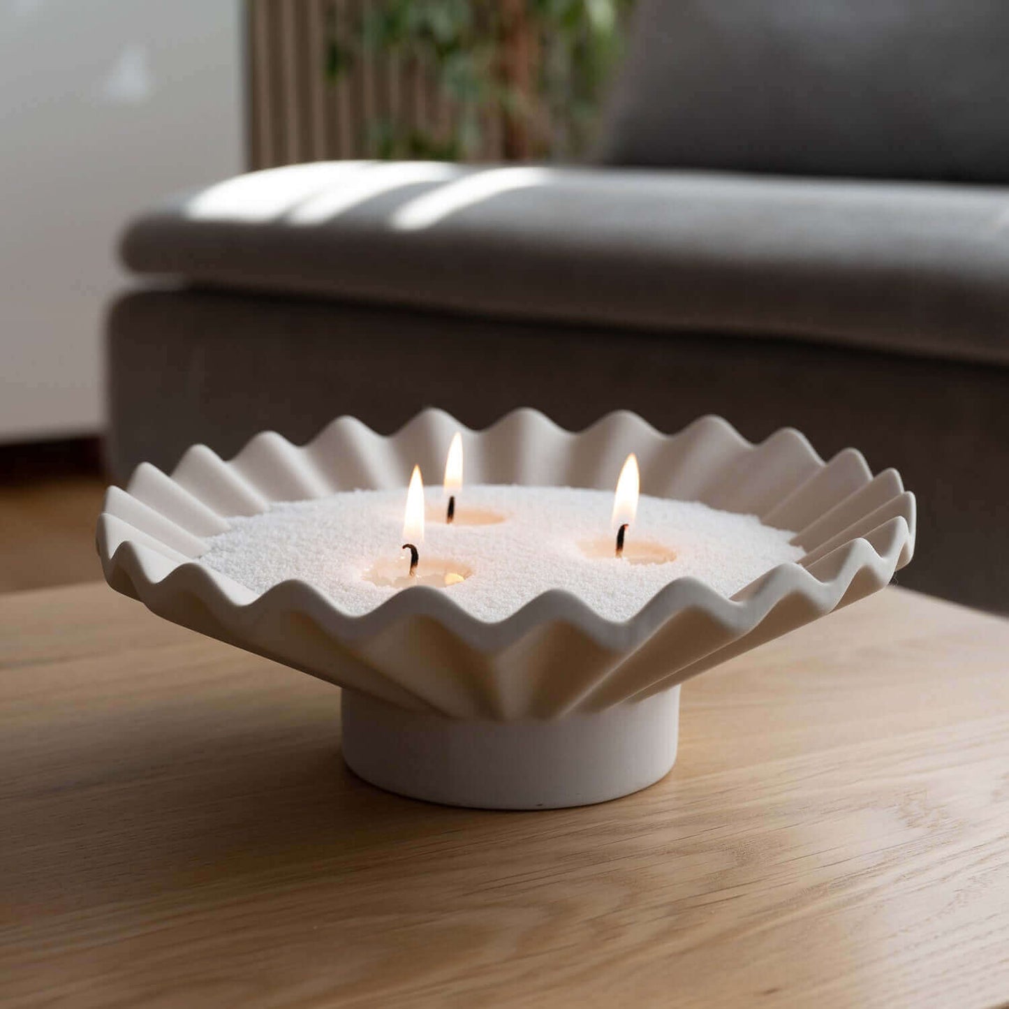 Bougie design Enora-Bougie dans un bol blanc plissé avec sable végétal blanc, trois mèches allumées, posée sur une table en bois pour une ambiance chic et naturelle.