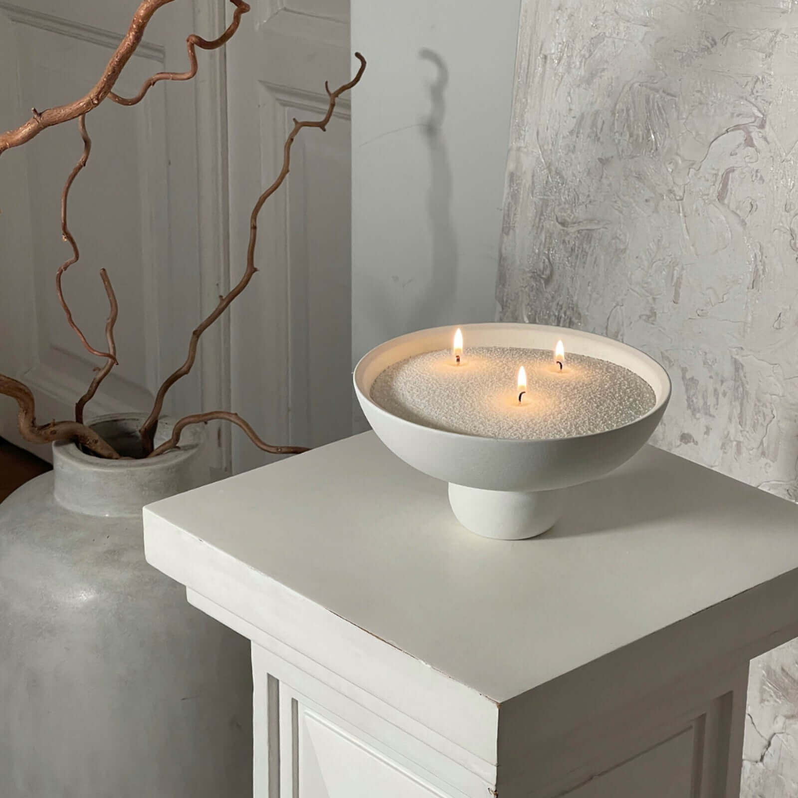 Bougie perlée Enora-Bougie dans un bol blanc moderne, posée sur un socle design, avec sable végétal et trois mèches allumées pour une ambiance zen et minimaliste.
